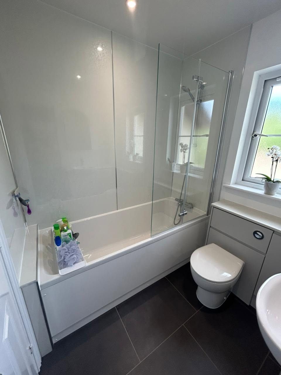Bath and shower suite with dark floor tiles